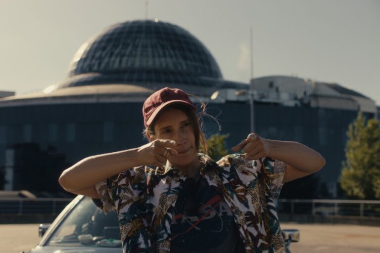 Kadr z filmu "Call me Lala". Kobieta unosi ramiona i pokazuje palcami przed siebie.