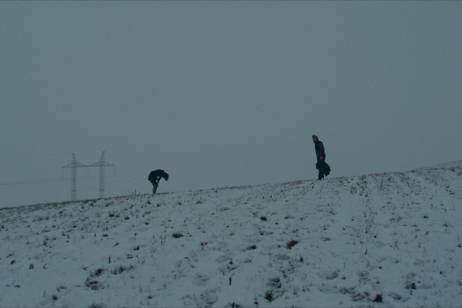 Kadr z filmu "Gone". Dwie postacie na przykrytej śniegiem łące. Jedna zgina się wpół.
