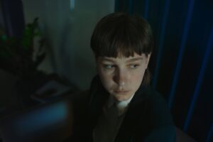 Kadr z filmu "Królowa Mrówek". Elegancko ubrana kobieta siedzi na kanapie. W pomieszczeniu panuje złowieszcza atmosfera.