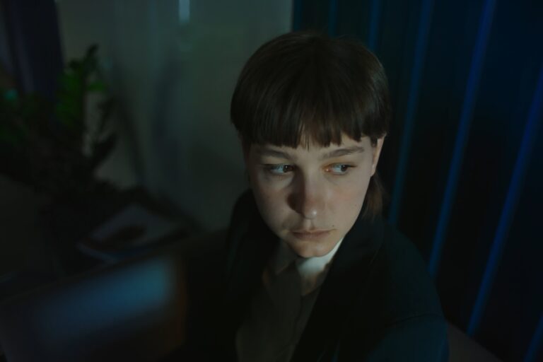Kadr z filmu "Królowa Mrówek". Elegancko ubrana kobieta siedzi na kanapie. W pomieszczeniu panuje złowieszcza atmosfera.