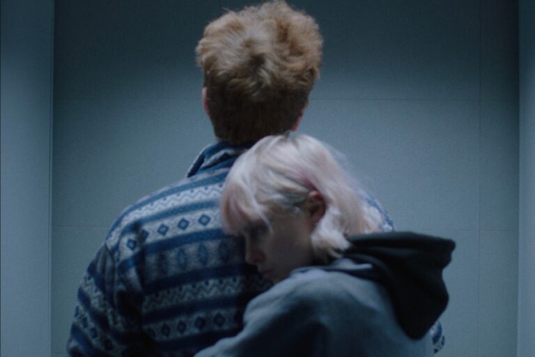 Kadr z filmu "No People Found". Kobieta obejmuje od tyłu mężczyznę, który stoi plecami do kamery.