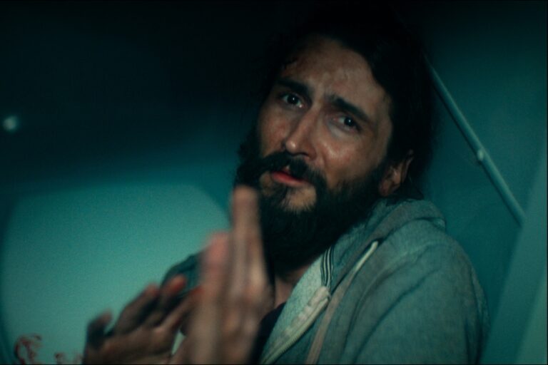 Kadr z filmu "Pilotka". Mężczyzna z błagalnym wyrazem twarzy wyciąga ręce w obronnym geście.